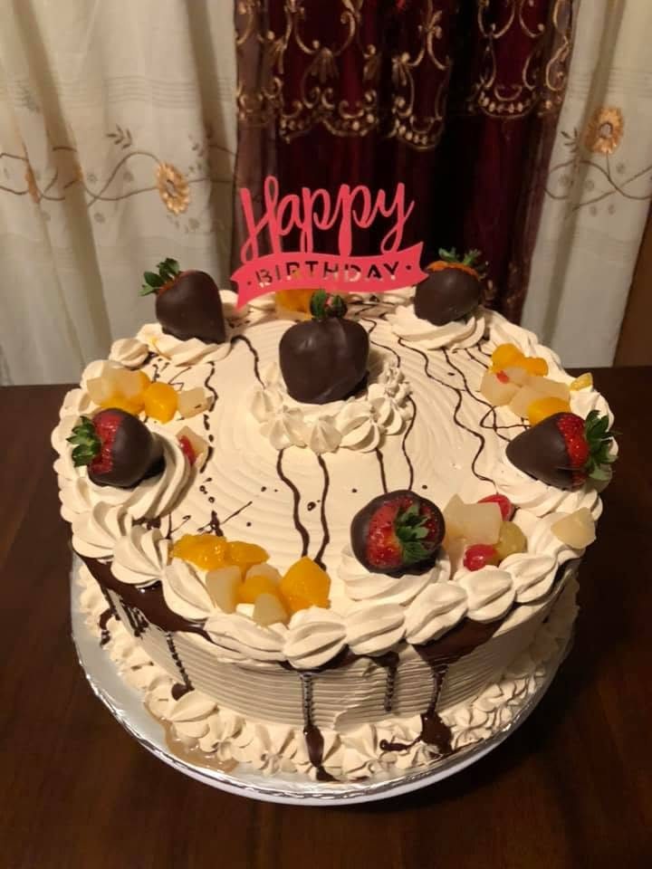 Cream cake topped with fruit and chocolate-dipped strawberries